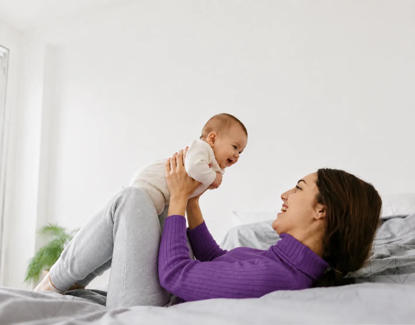 Mother lifting and smiling at her baby on a bed