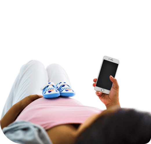 Pregnant mother holding a phone with baby shoes resting on her belly